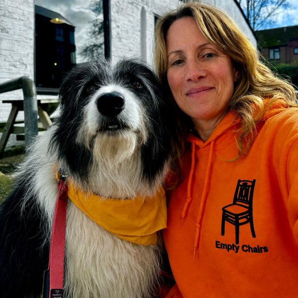 Nicole in an orange Empty Chairs hoodie, with her dog Storm beside her.